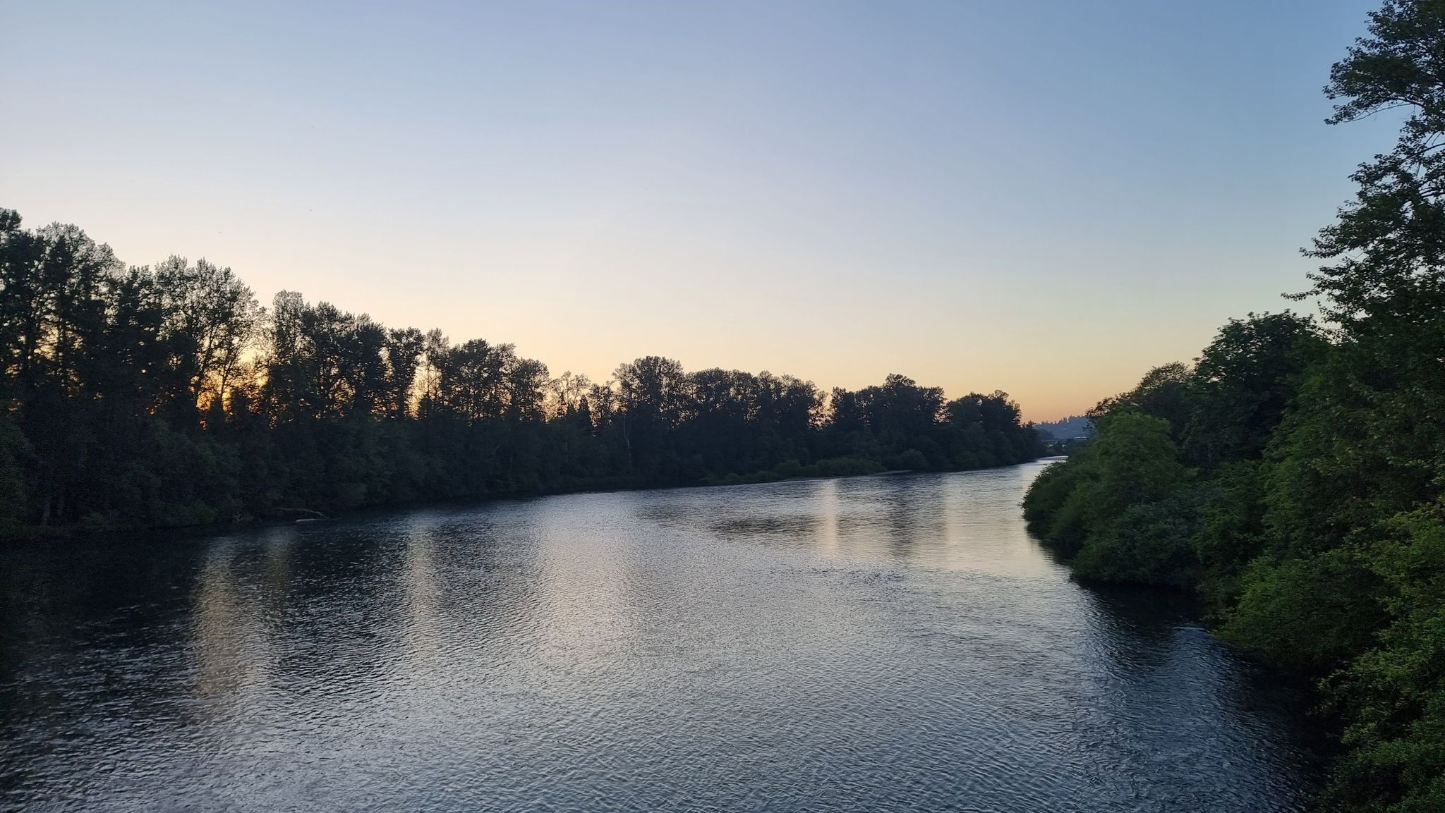 A wide river at dusk, flanked by dark trees under a fading sky. - Ruth Bascom Path loop