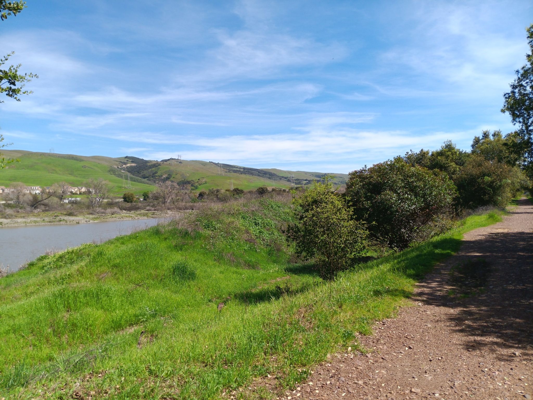 Dirt path beside a lake, green grassy hills, and distant mountains. - Coyote Creek Loop