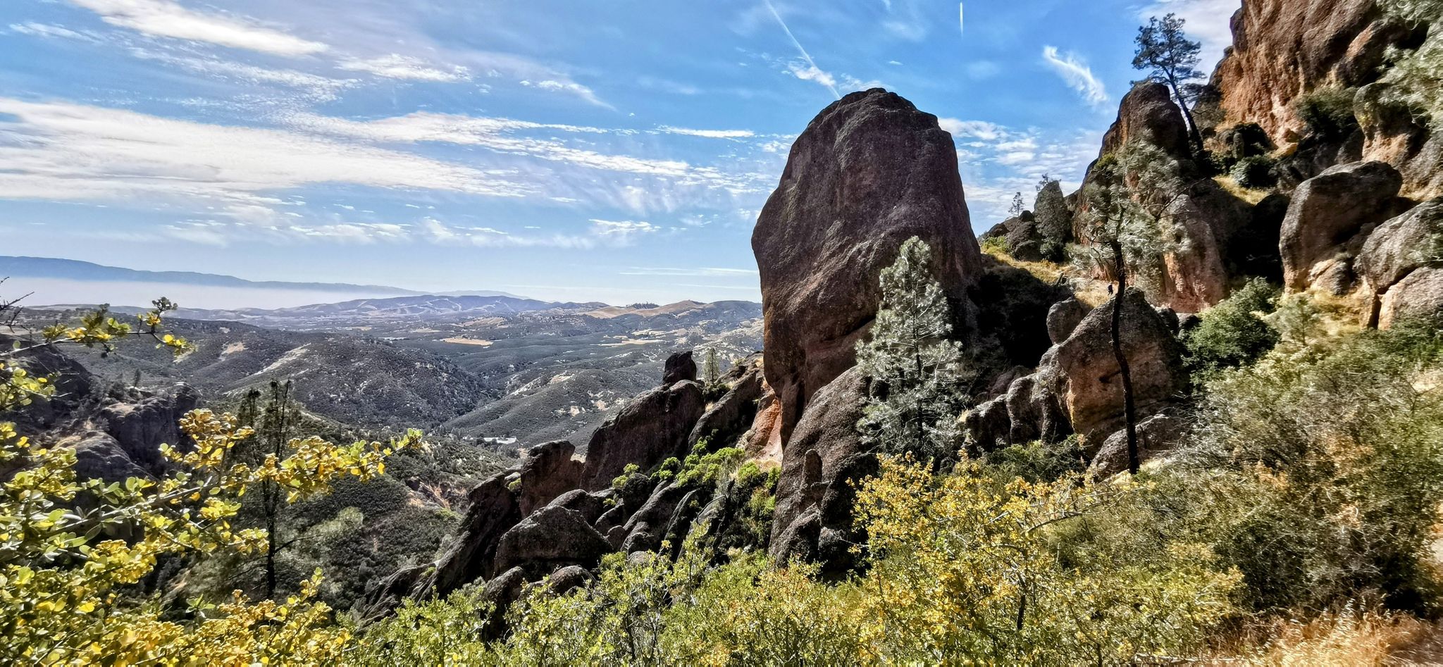 Majestic rock formations overlook a vast, hazy valley under a bright blue sky. - Condor Gulch to High Peaks Loop
