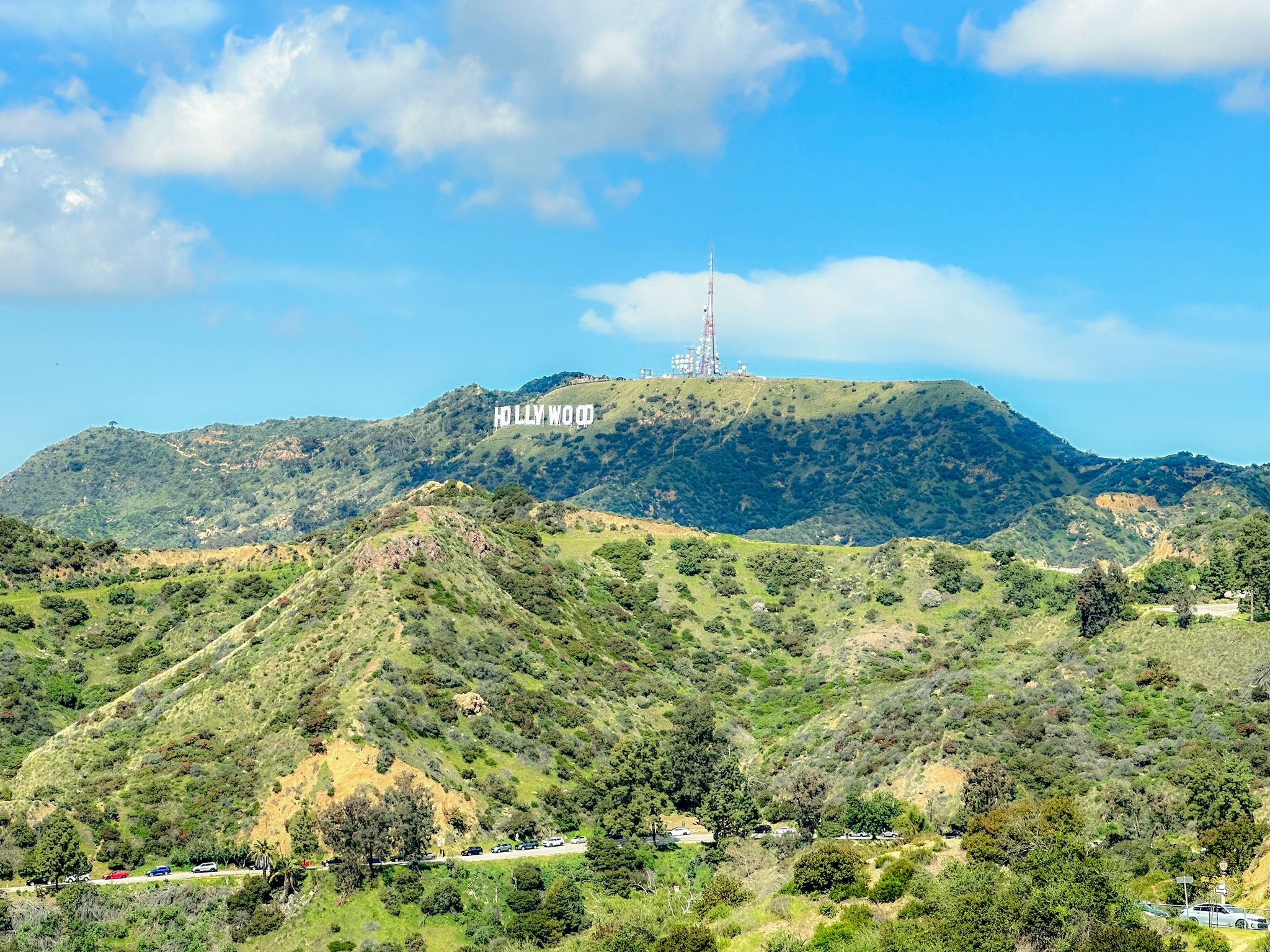 Distant white letters on a green hillside under a bright, cloudy sky. - Griffith Park loop