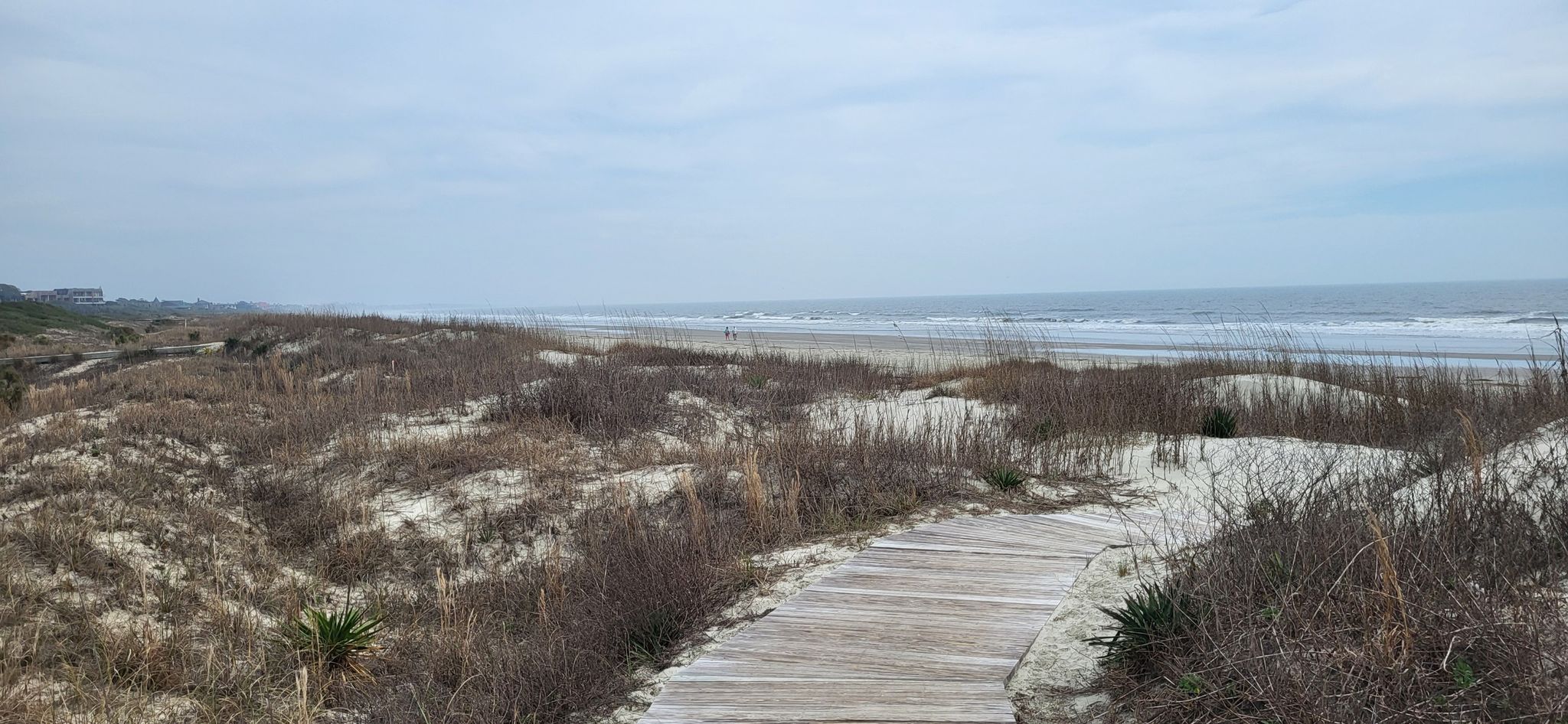 Wooden boardwalk through sandy dunes leads to a wide, overcast beach and ocean. - Kiawah Island Beach Walk