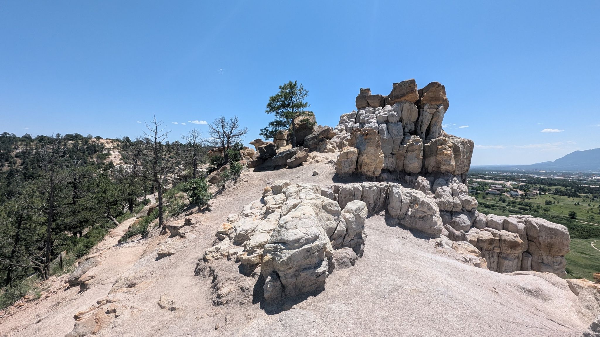 A prominent rocky outcrop with a lone tree under a bright blue sky. - Pulpit Rock Trail