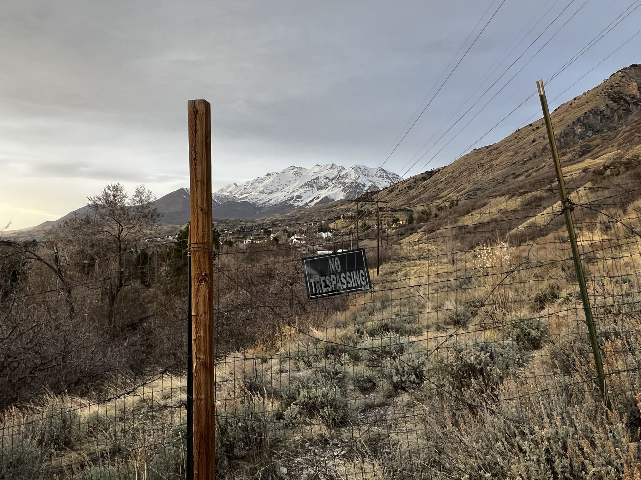 A 'No Trespassing' sign on a fence with a snowy mountain under an overcast sky. - Bonneville Shoreline Trail: Rock Canyon Park Connector