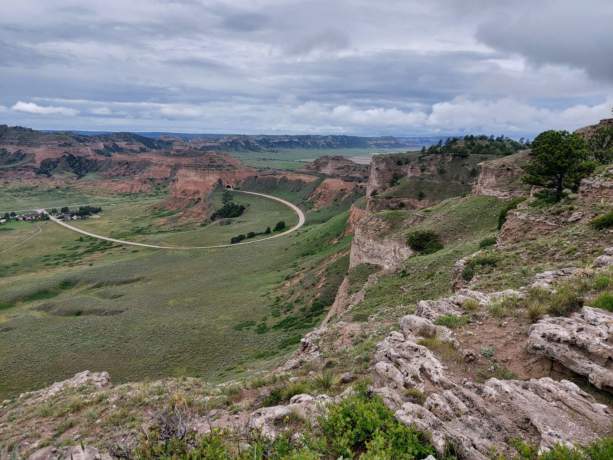 Overcast view of a green valley with a winding road and rocky cliffs. - Saddle Rock Trail
