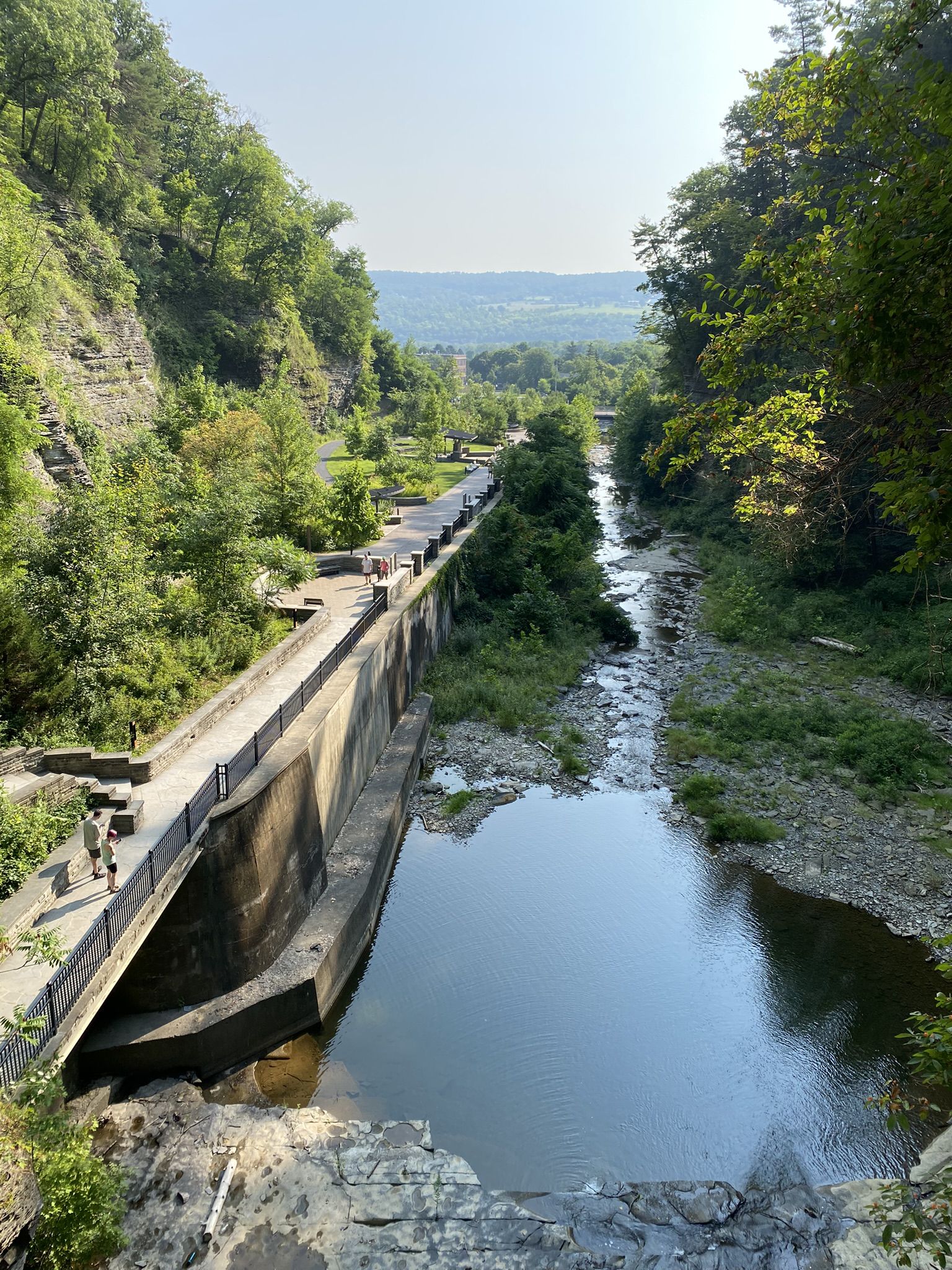 Sunny view of a river flowing through a gorge with a paved path and people. - Gorge and Indian Trail Loop