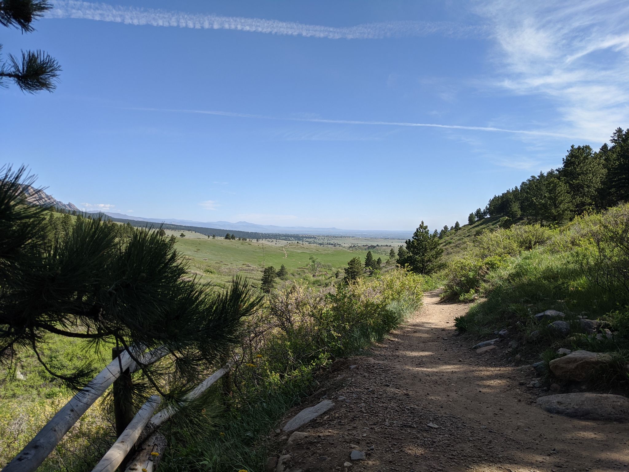 Sunny dirt trail overlooking a vast green valley and distant mountains. - Doudy Draw Trail