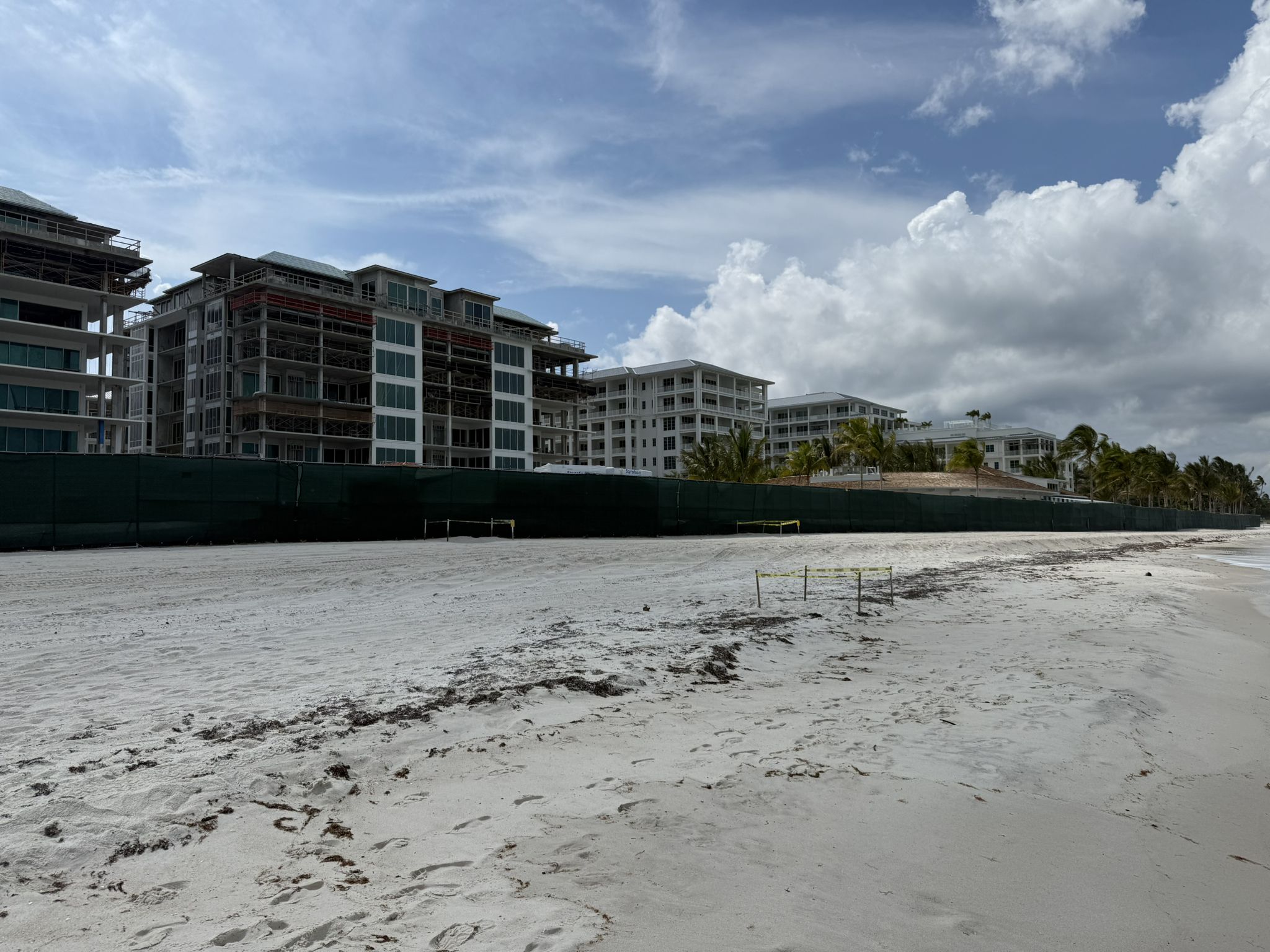 Sandy beach with buildings under construction behind a green fence, cloudy sky. - Lowdermilk Park Beach loop