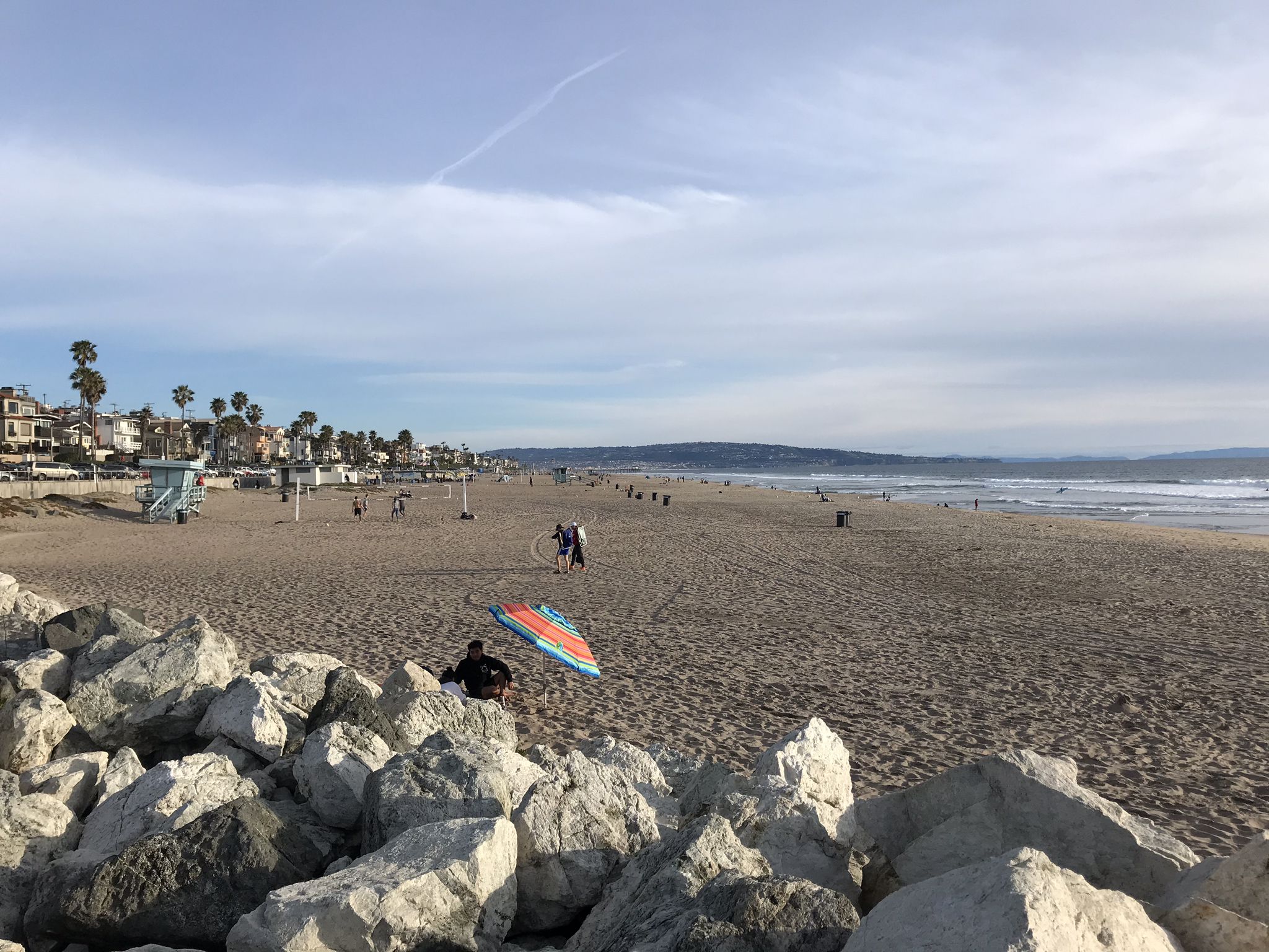 Wide sandy beach with people, ocean, and distant buildings under a bright sky. - El Segundo Beach – El Segundo Beach loop from Manhattan Beach