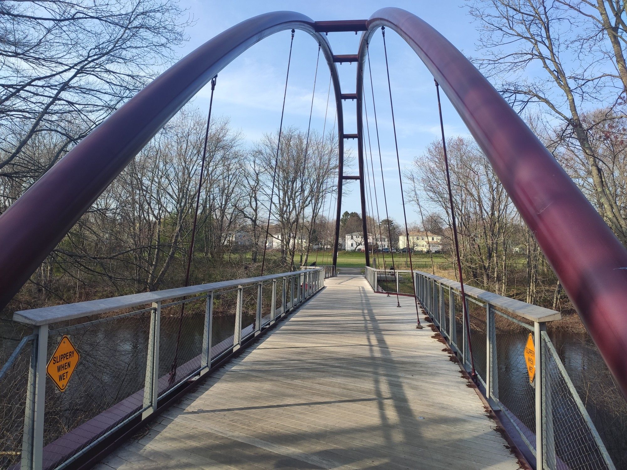 A red arched pedestrian bridge spans over water, surrounded by bare trees. - Walking City Trail: Section 1