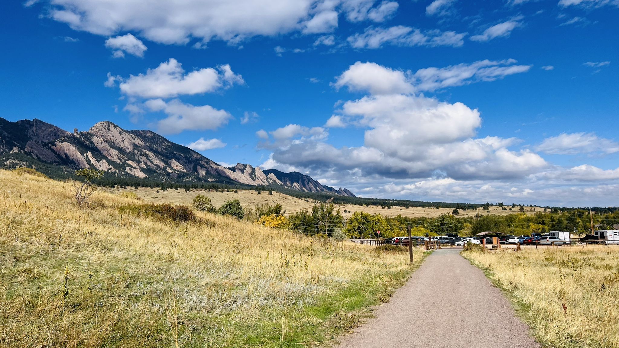 A dirt path leads through dry fields towards mountains under a bright sky. - Doudy Draw and Flatirons Vista Loop
