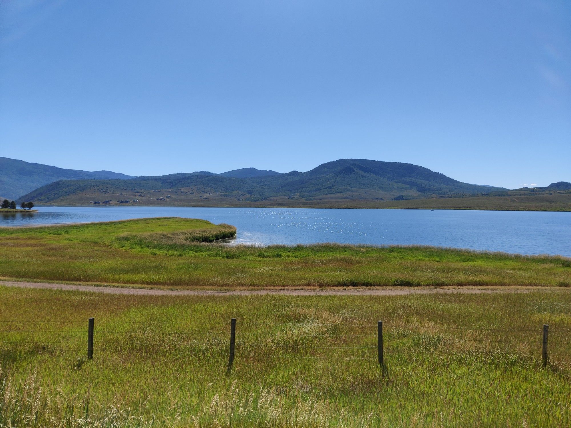 A wide blue lake with green fields and distant mountains under a clear sky. - Stagecoach Reservoir & Oak Creek loop