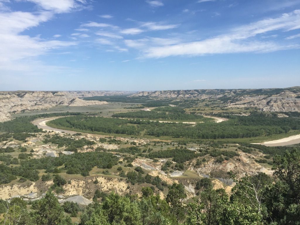 Expansive view of a winding river through a green valley and badlands under a blue sky. - Achenbach Trail Loop