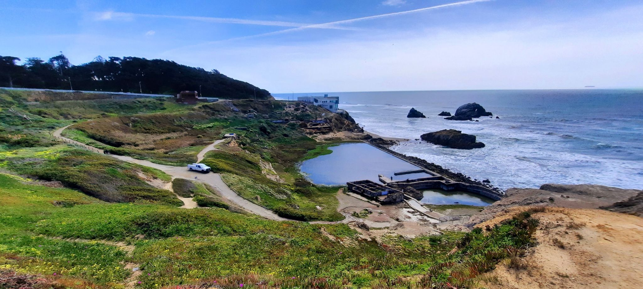 Coastal landscape with ocean, rocky shore, and a large pool, under blue sky. - HikANation Historical Route