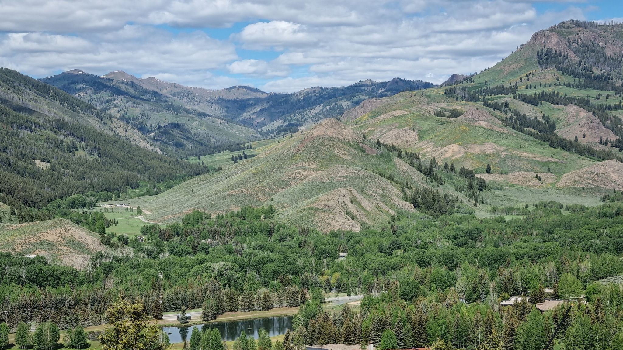 Expansive mountain valley with green hills, dense forests, and a calm lake. - Sun Valley Village loop from Sun Valley