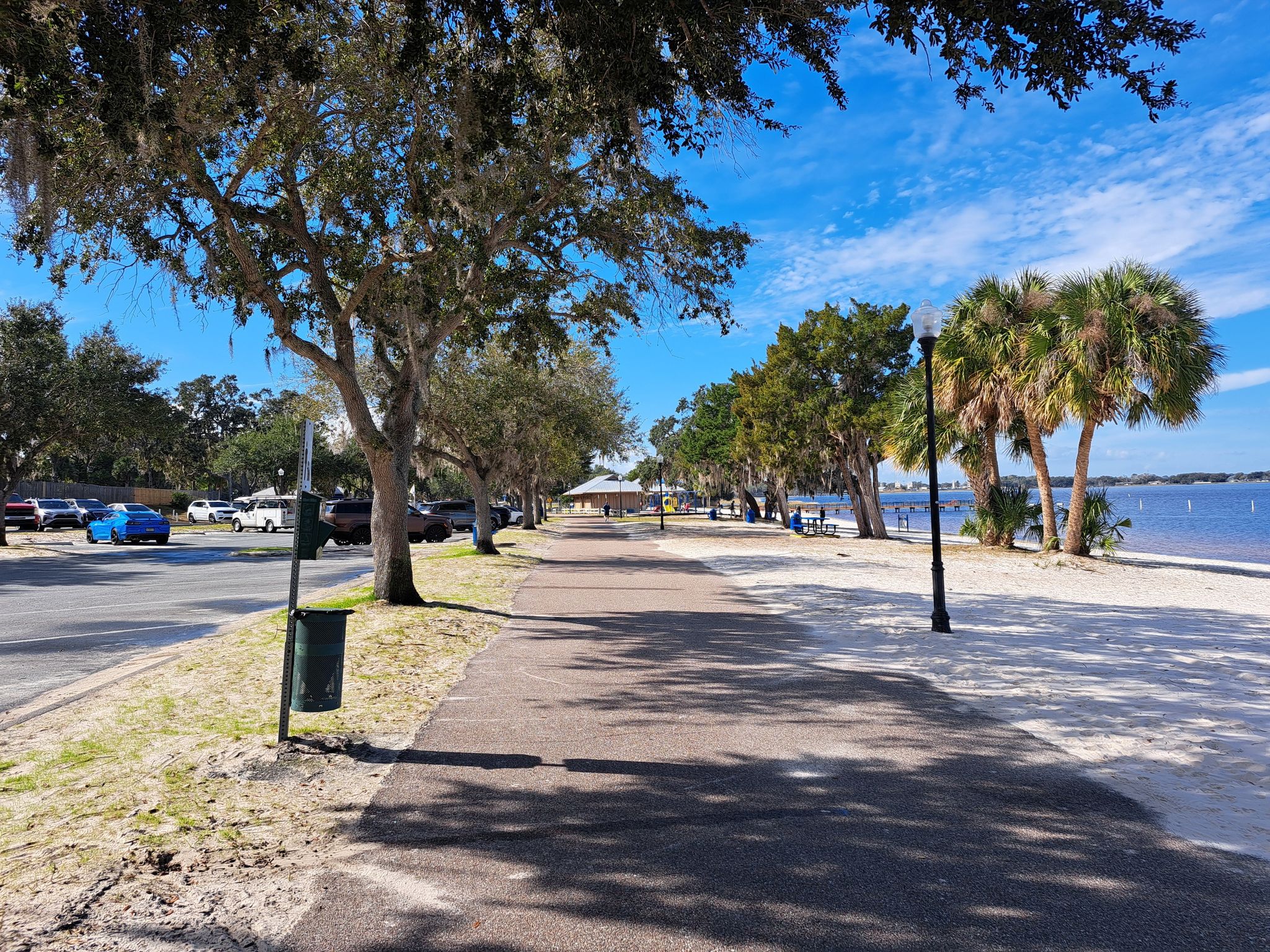 Paved path and road alongside a sandy beach and lake. - South Lake Trail – West Orange Trail loop from Lake Louisa State Park