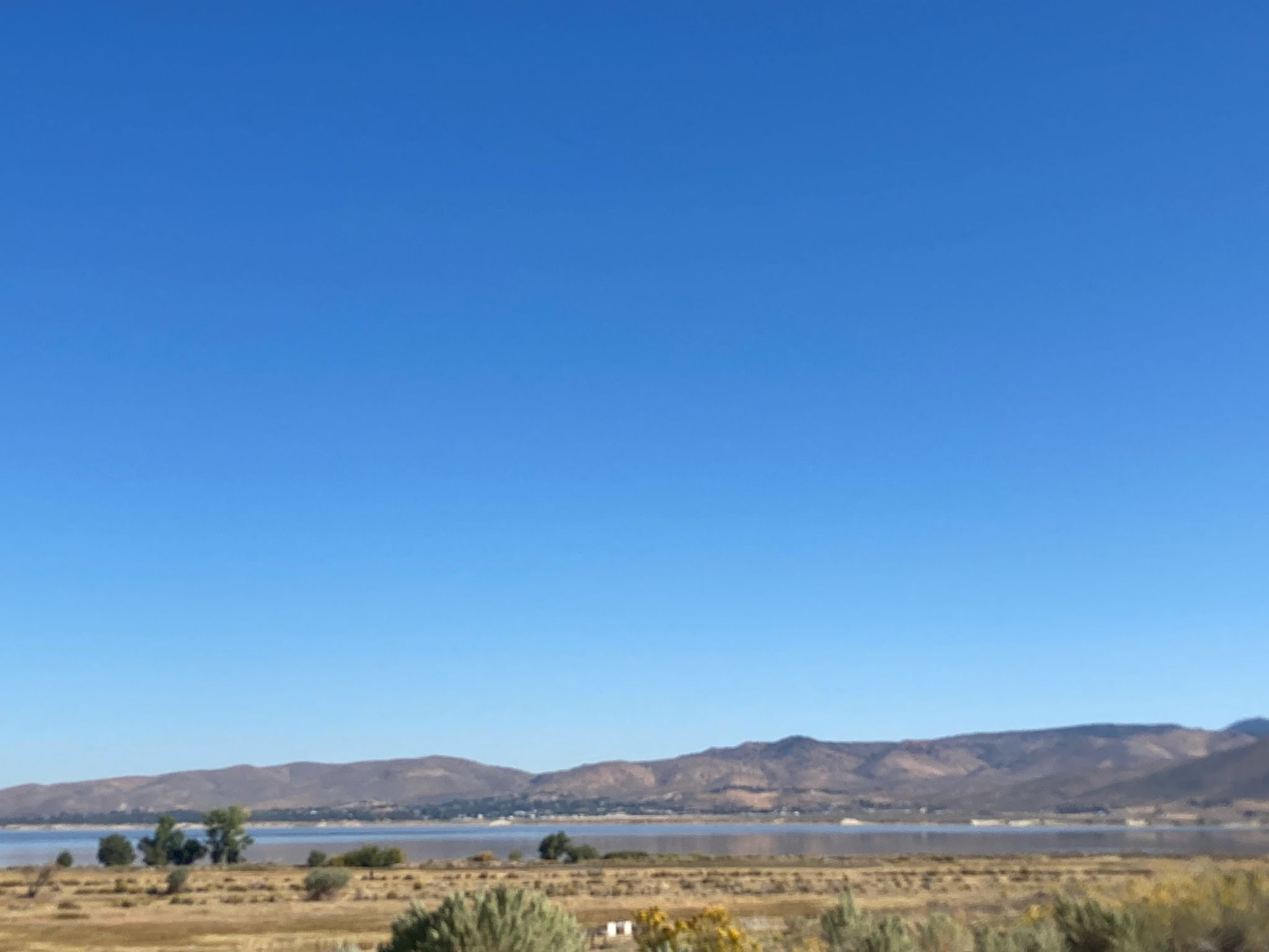 Expansive view of a calm lake, dry plains, and distant mountains under a clear sky. - Washoe Valley Loop