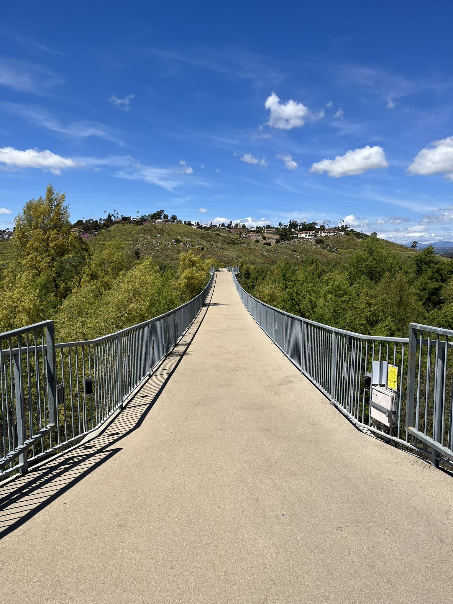 Long, empty pedestrian bridge over green hills under a blue sky. Bright sun. - Lake Hodges loop from Bernardo Winery