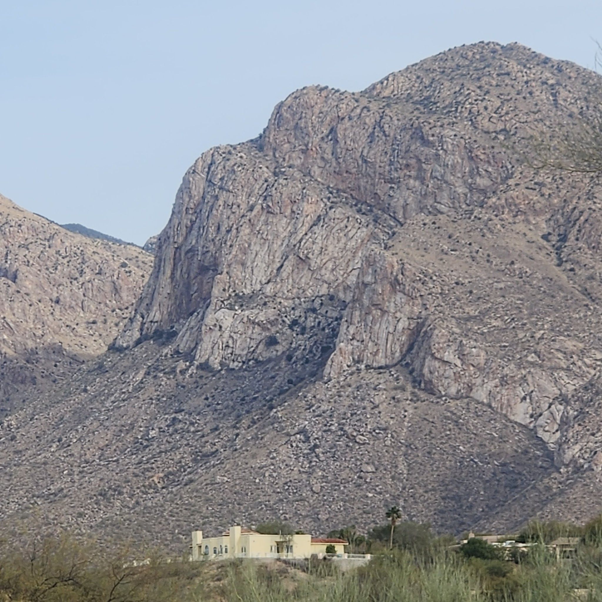 Close-up of a massive, rocky mountain face with a house nestled below. - Cañada del Oro River Trail – Cañada del Oro River Park loop from Ina/Thornydale