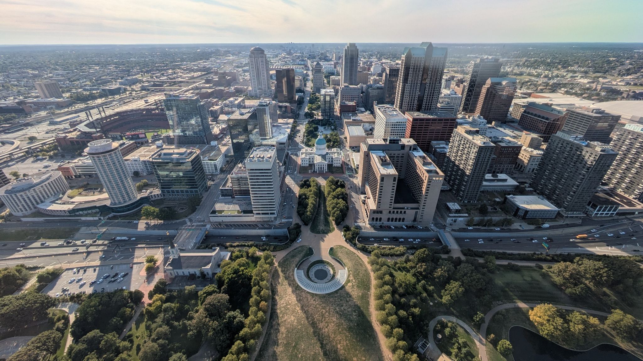 Aerial view of a sprawling city with skyscrapers, parks, and a distant river. - Luther Ely Smith Square – Eads Bridge loop from Union Station