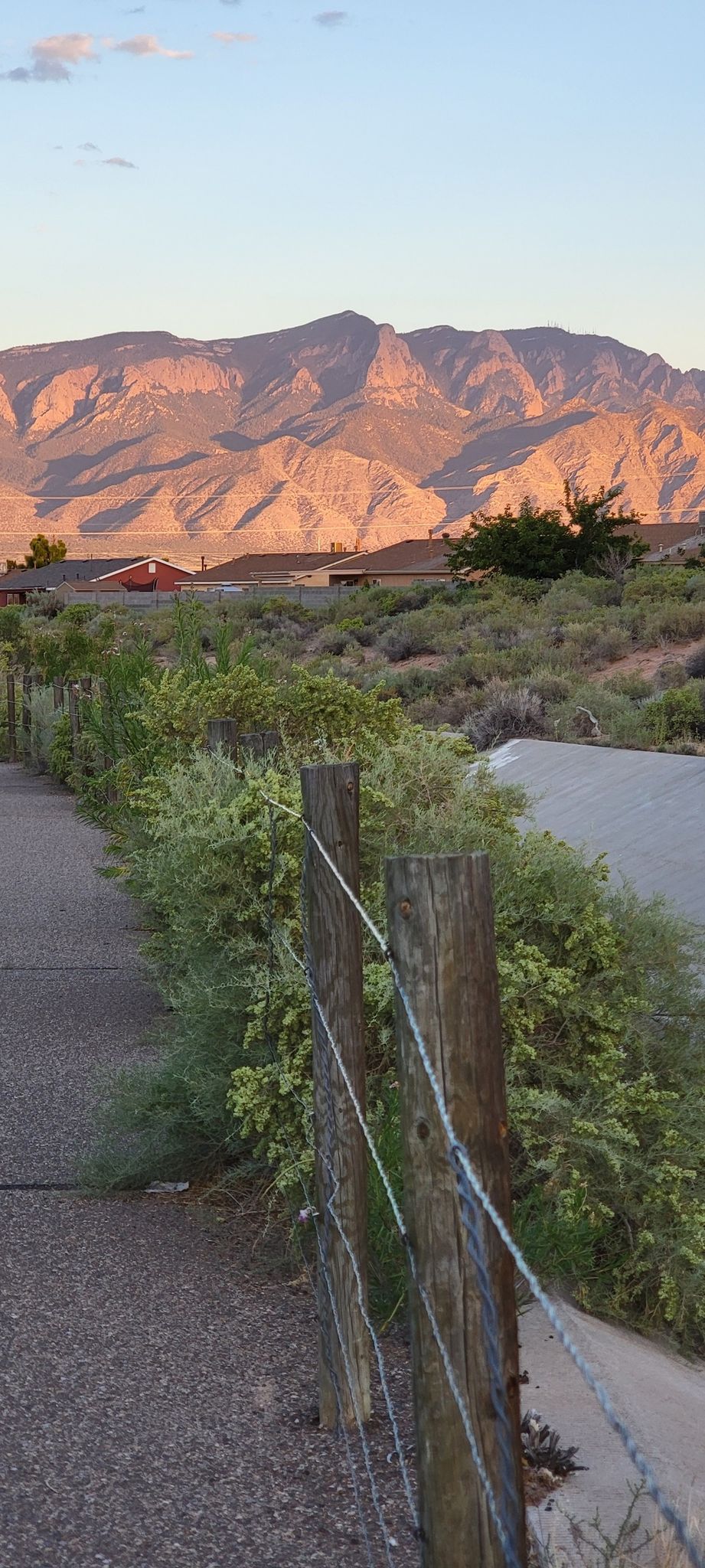 Wooden fence next to a path with sunlit mountains in the background. - Enchanted Hills Trail
