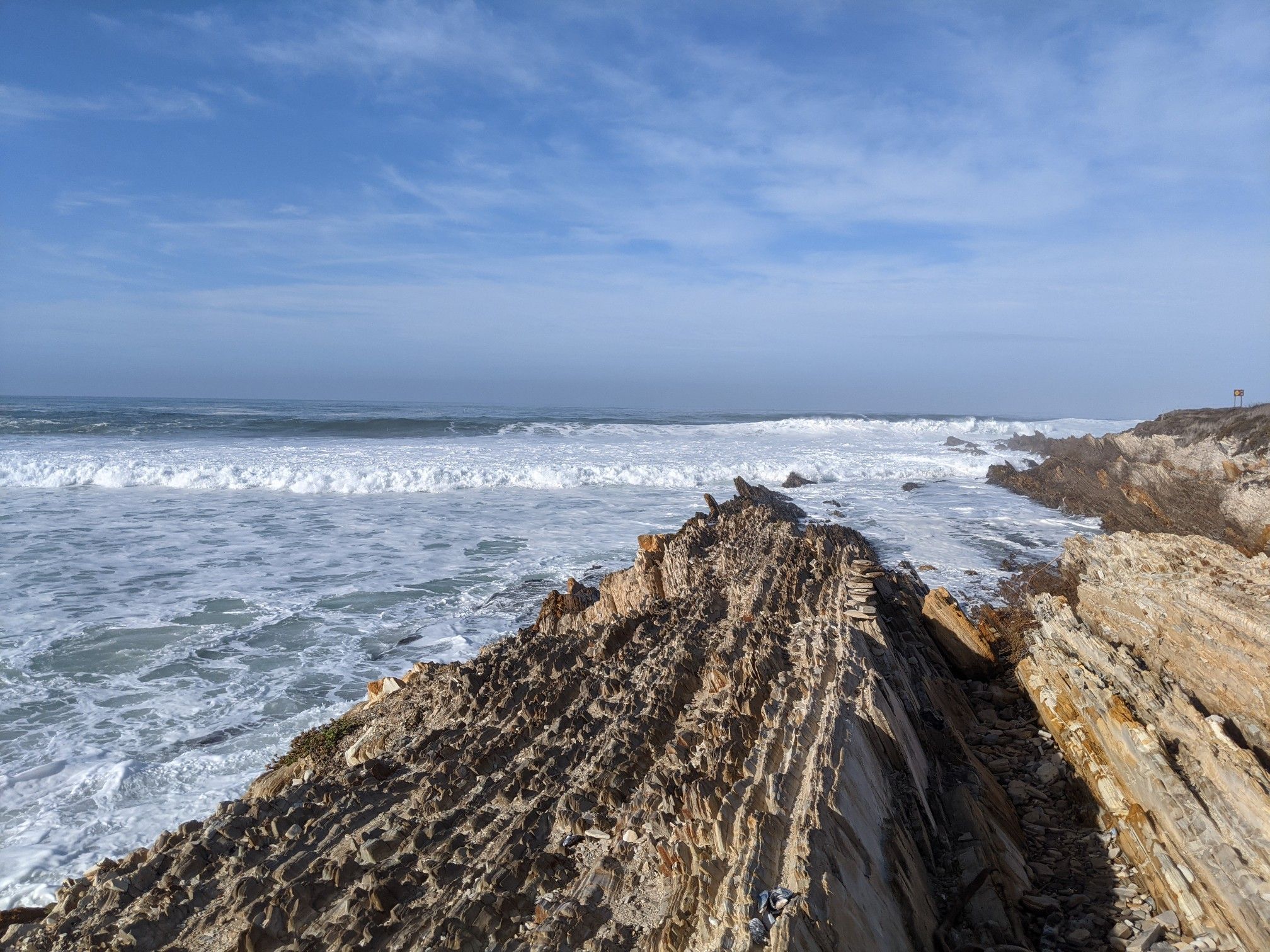 Rocky coastline with foamy waves under a blue sky. - Montaña de Oro Bluff Trail