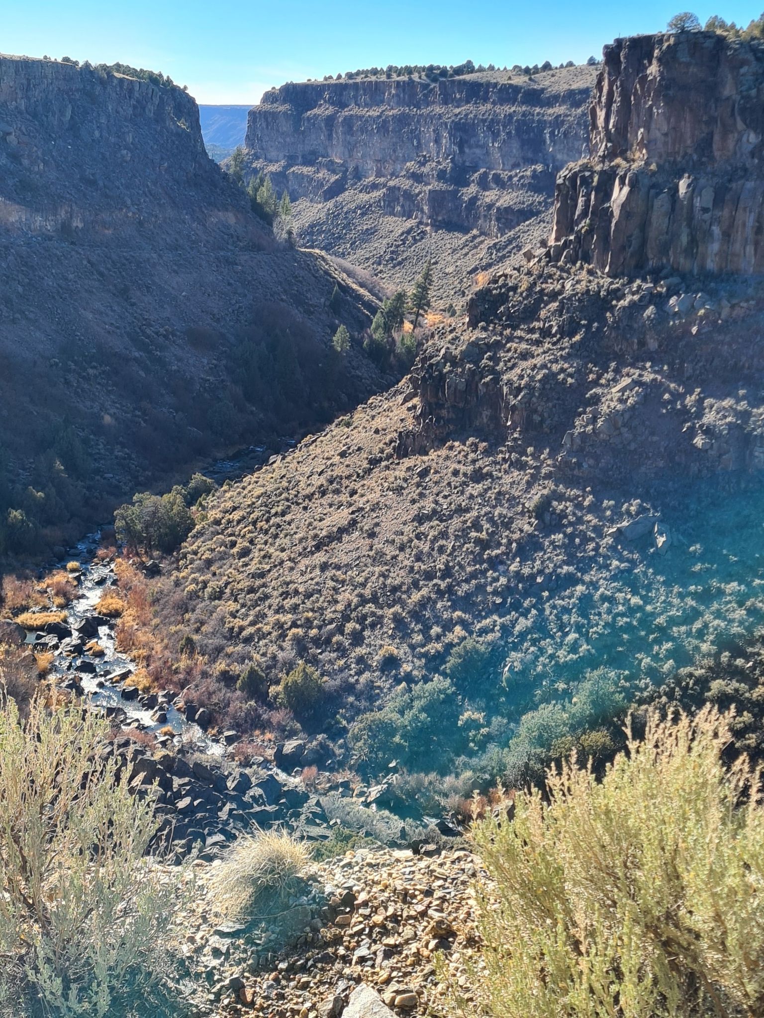 Wide canyon view with a river, rocky slopes, and dry brush under clear sky. - Picuris, Klauer, and Slide Trail Loop