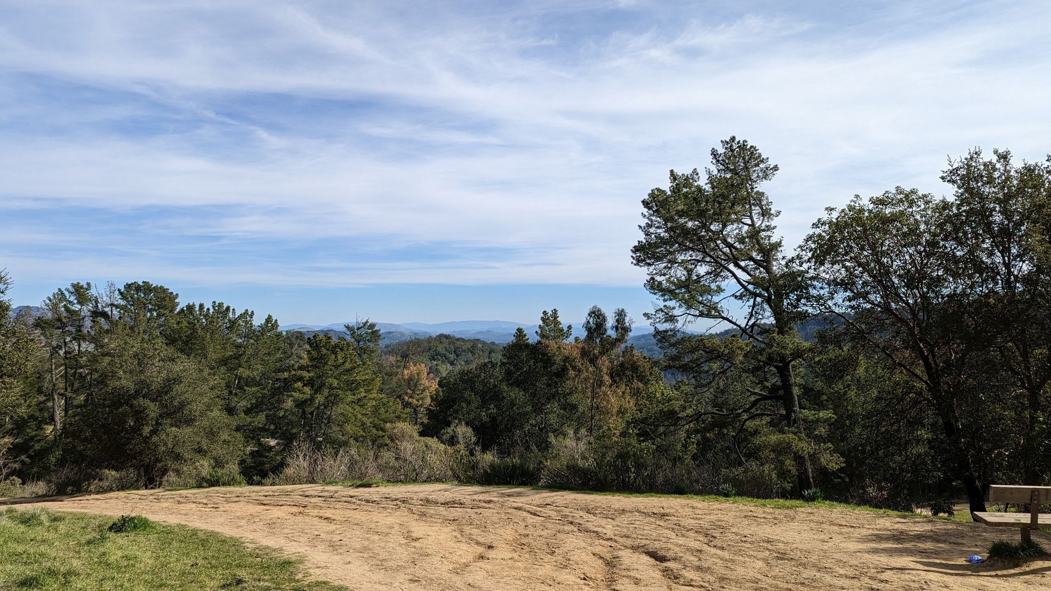 An open dirt clearing overlooks distant forested hills under a partly cloudy sky. - Stream, East Ridge, and Canyon Loop