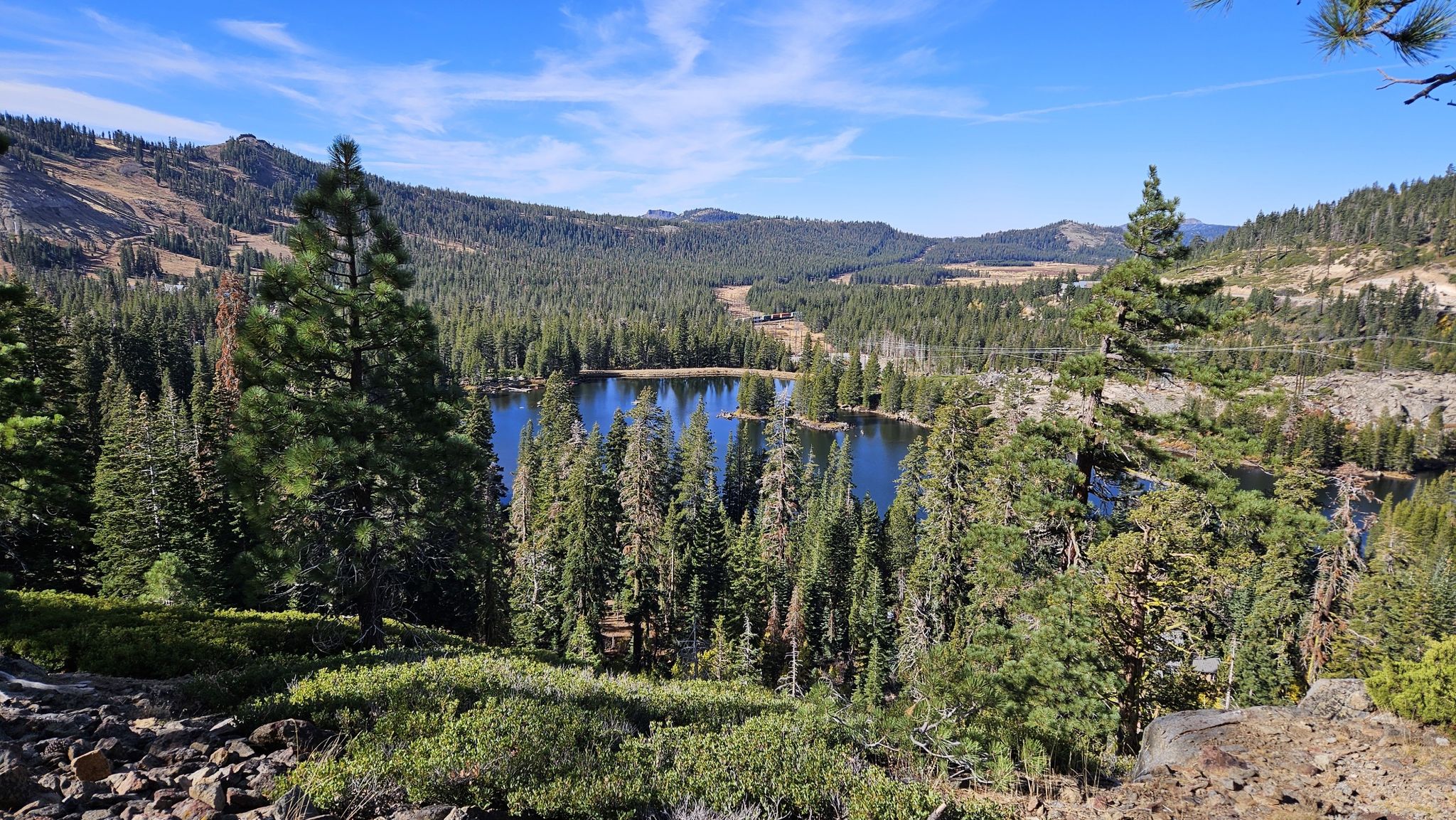 A clear blue lake surrounded by dense pine forests and mountains under a sunny sky. - Donner Pass to Olympic Valley via the Pacific Crest Trail