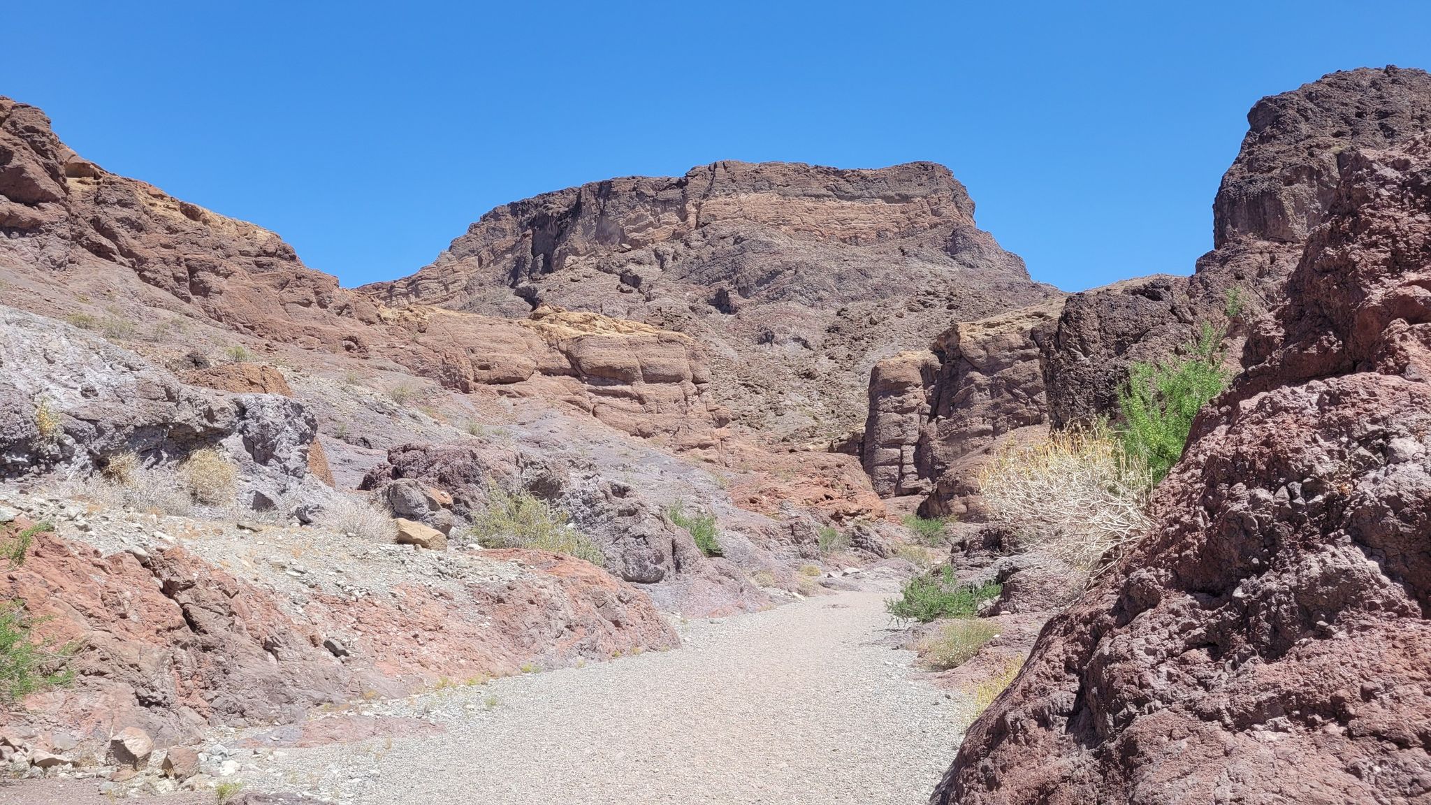 Dry, sandy wash leading through a canyon with towering rocky walls under a clear sky. - Arizona Hot Spring Trail