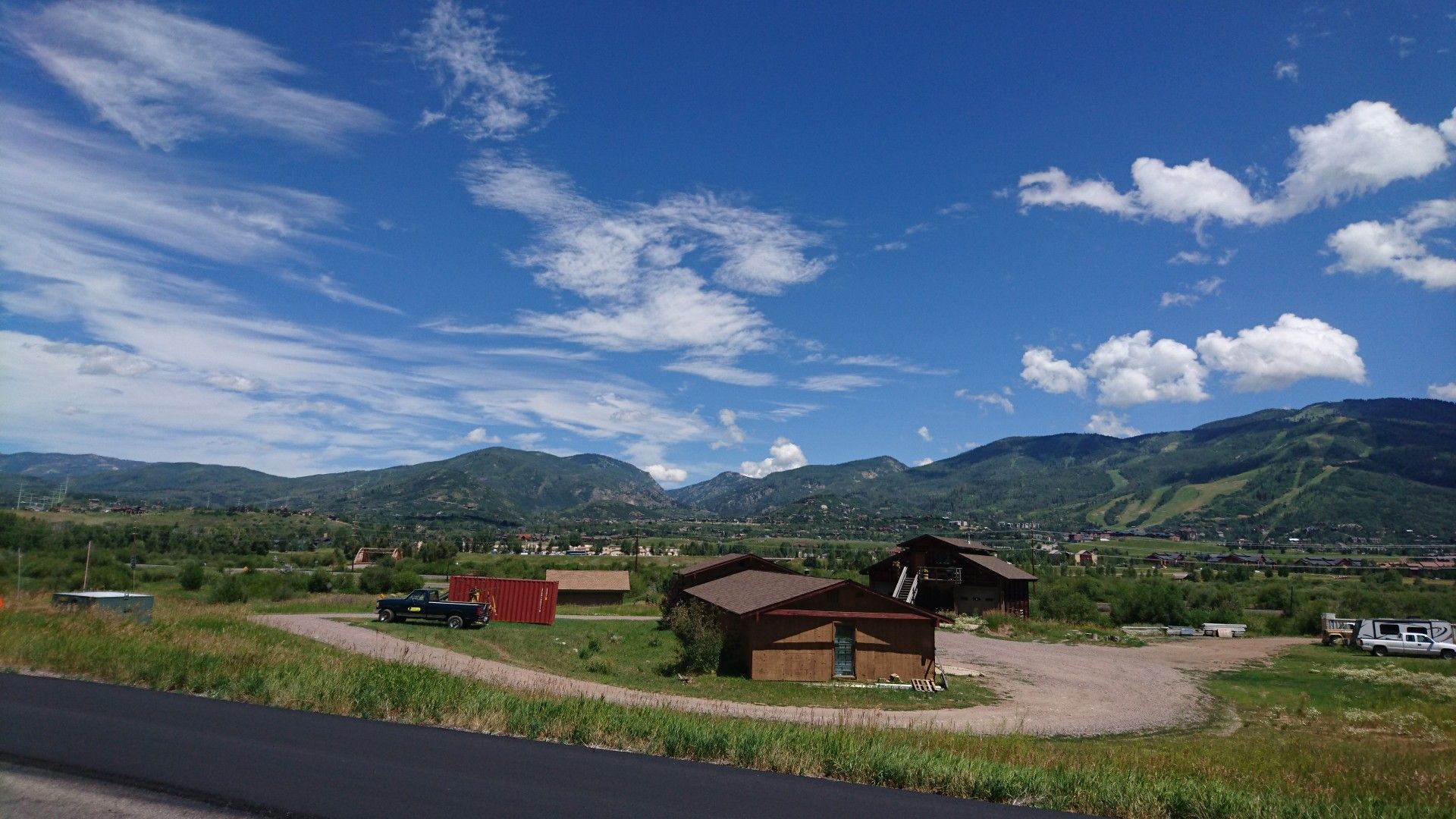 Rural homes in a green valley with majestic mountains under a blue sky. - Oak Creek loop