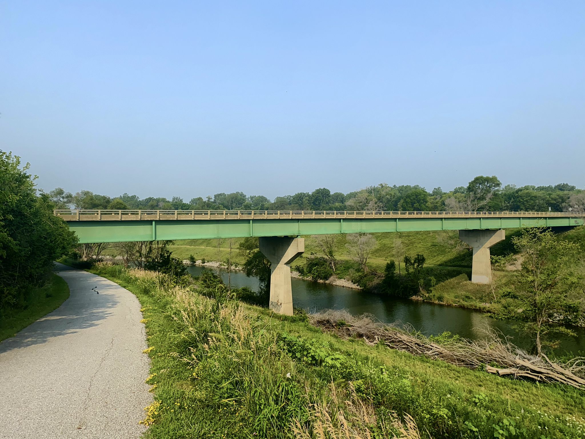 A green bridge spans a river with a paved path and green foliage. - Neal Smith Trail