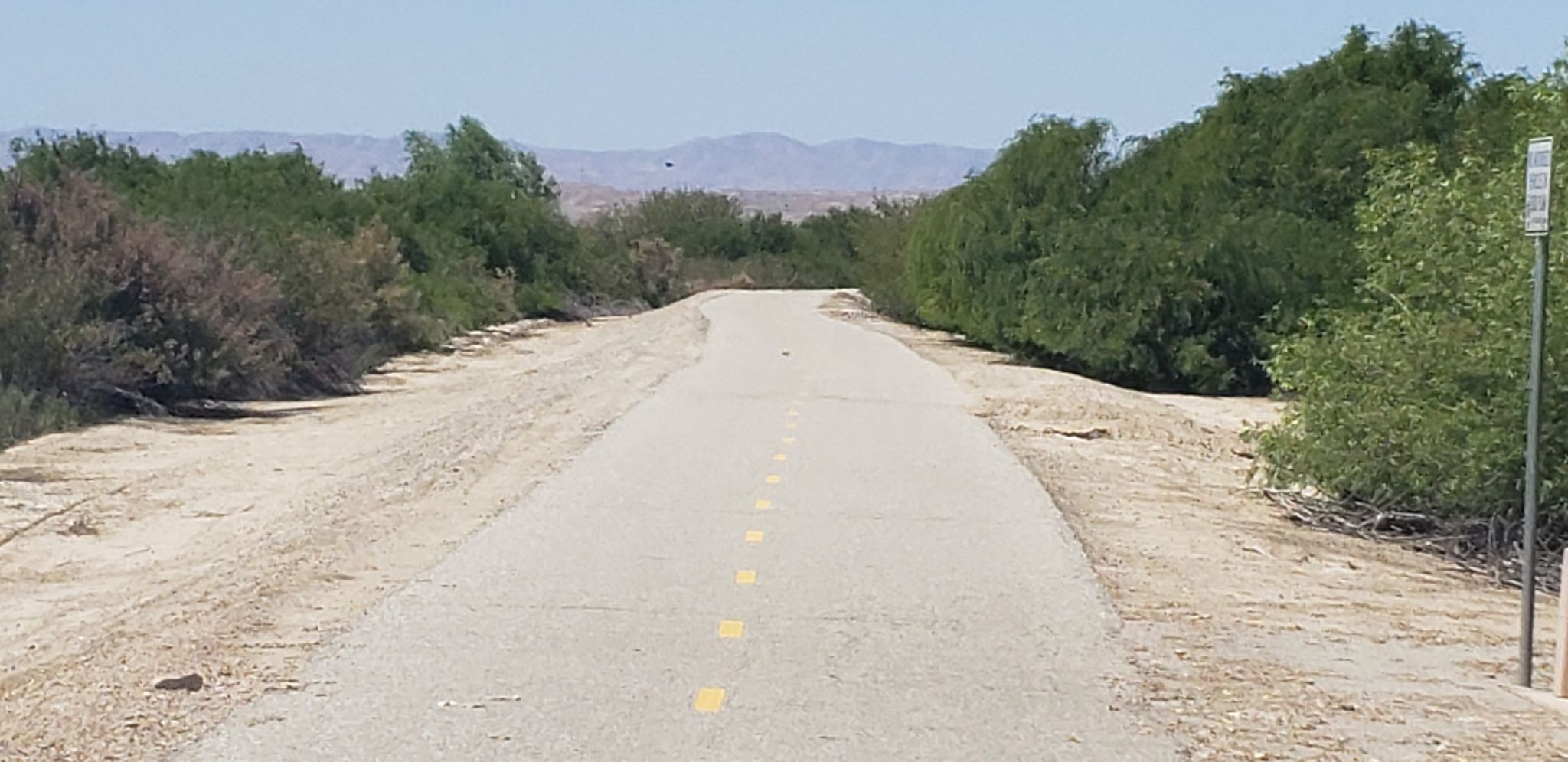 Paved path through desert brush under a clear sky with distant mountains. - Kern River Parkway Trail
