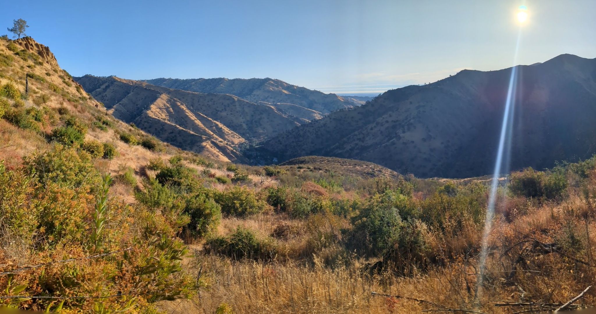 Sunny mountain valley with dry brush in the foreground and lens flare. - View of Lake Berryessa loop from Morning Glory Spillway Opening