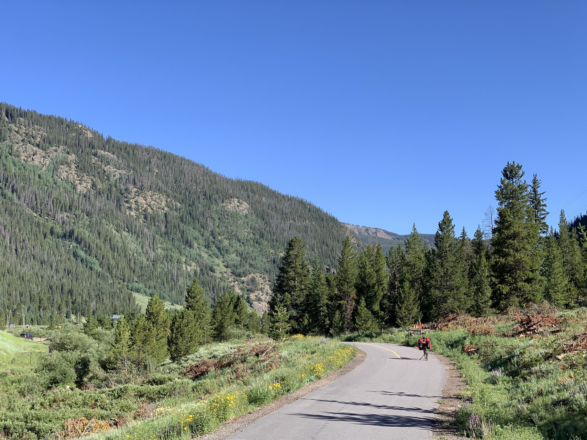 Cyclist on a paved road through a green valley with forested mountains. - Frisco – Copper Mountain loop from Passage Point