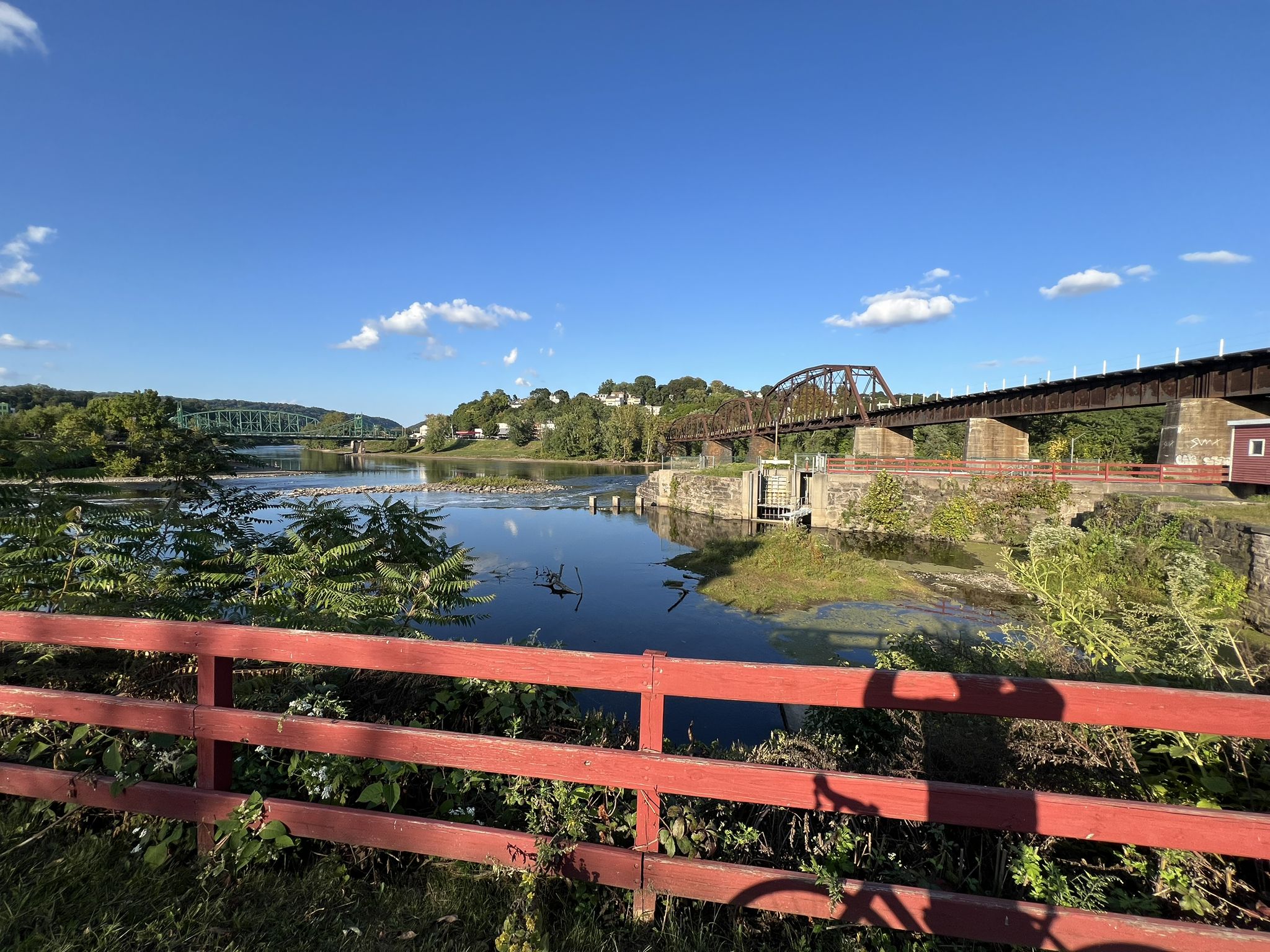 A river with multiple bridges in the distance, viewed over a red fence. - Delaware Canal State Park – Saucon Rail Trail loop from Saucon Valley Country Club
