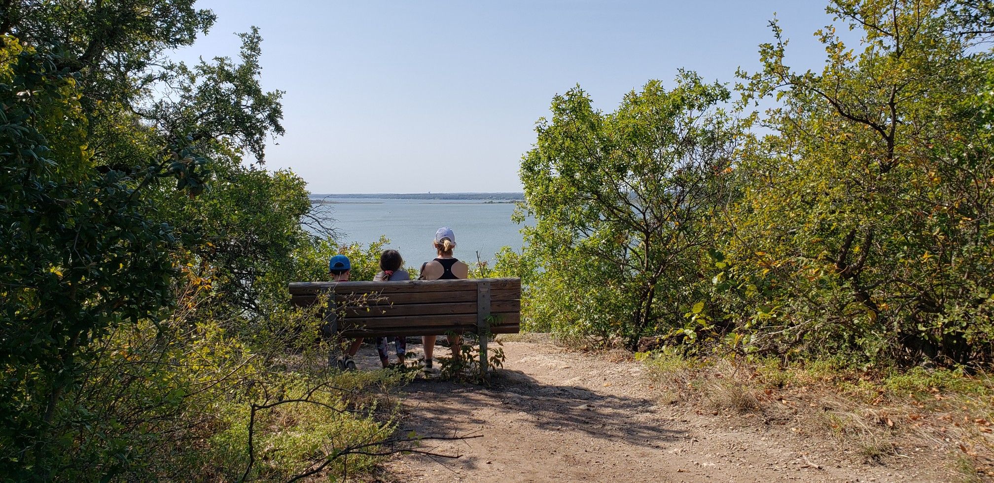 Three people sit on a bench, enjoying a sunny view of the water. - Eagle Mountain Northwest Loop