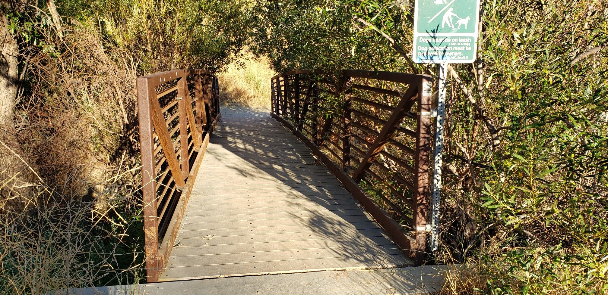 Small metal bridge with concrete path surrounded by dry brush in bright sunlight. - Aliso Canyon Trail