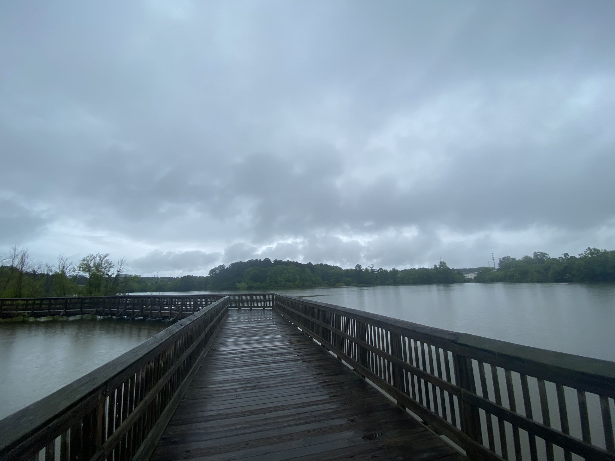A long wooden boardwalk extends over a calm lake under an overcast sky. - Raleigh Greenway: Crabtree and Walnut Creek Loop