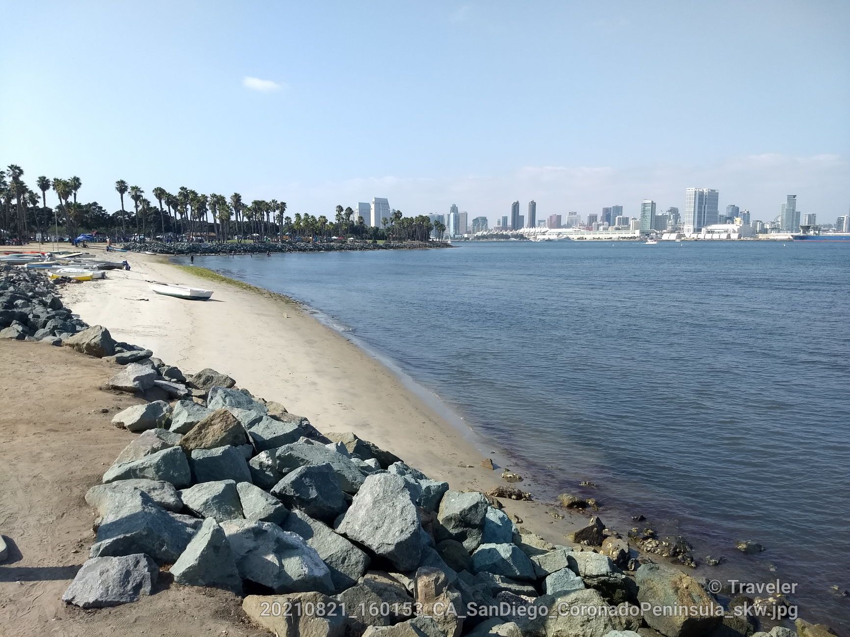 Rocky and sandy beach by calm water with a distant city skyline. - Bayshore Bikeway: Centennial to Tidelands Park