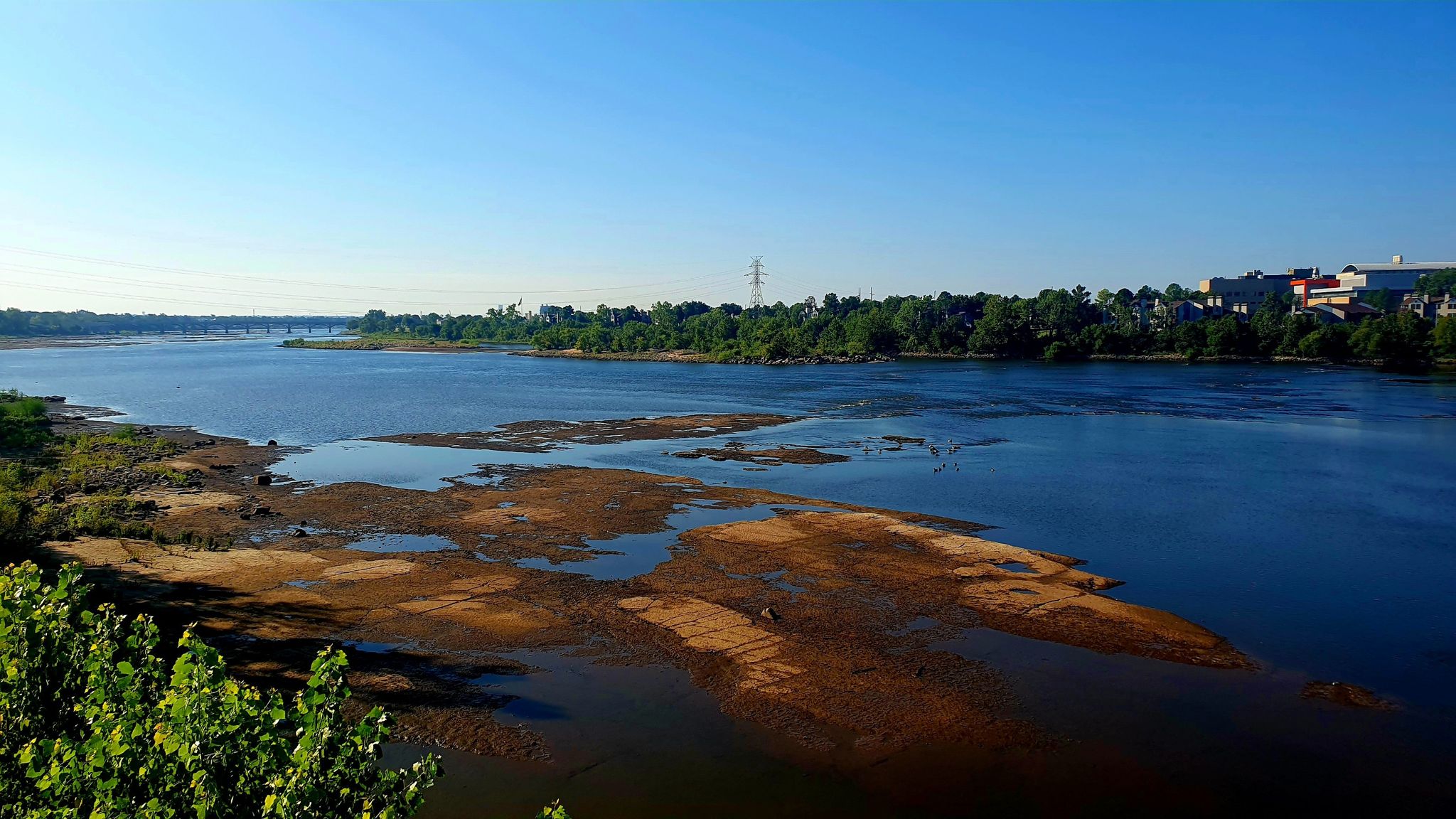 Wide river with sandy banks and distant city buildings under a clear sky. - Route 66 to Sapula