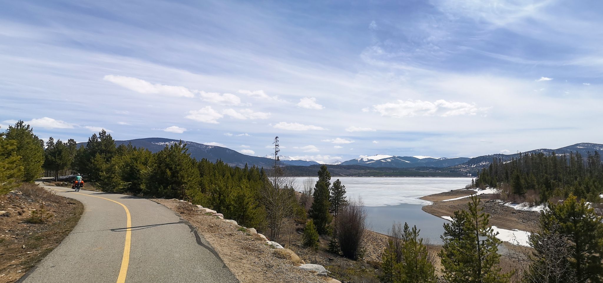 Cyclist on paved path beside a partially frozen lake and snowy mountains. - Dillon Reservoir Recpath Loop