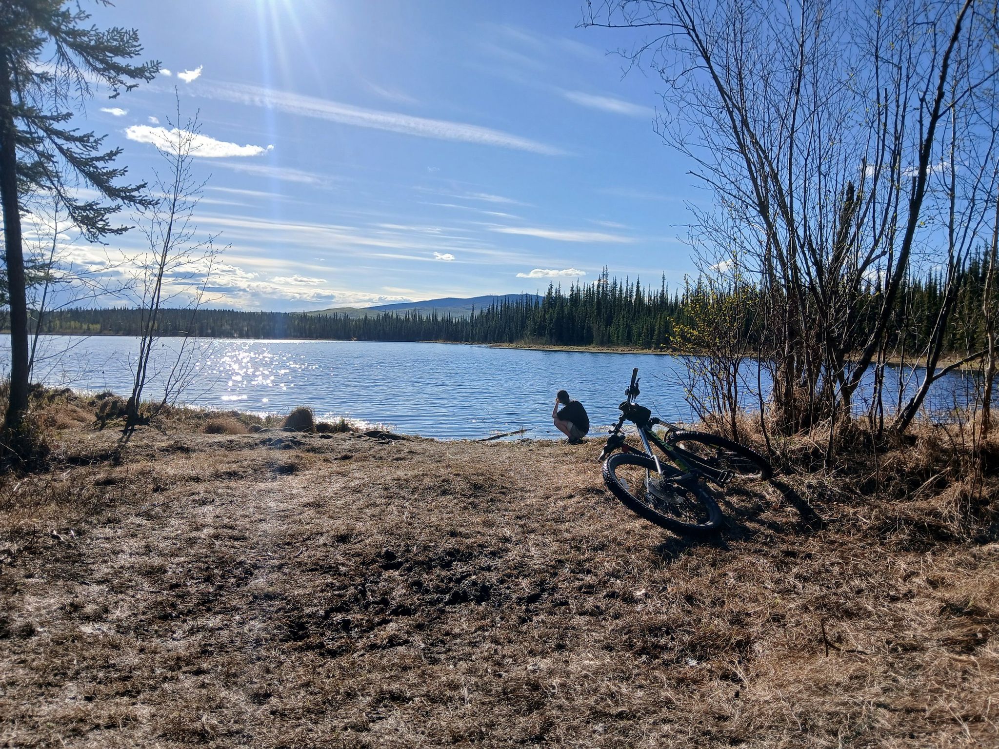 A person sits by a lake with a bicycle on a sunny day. - Sheep Creek  to Goldstream Road loop