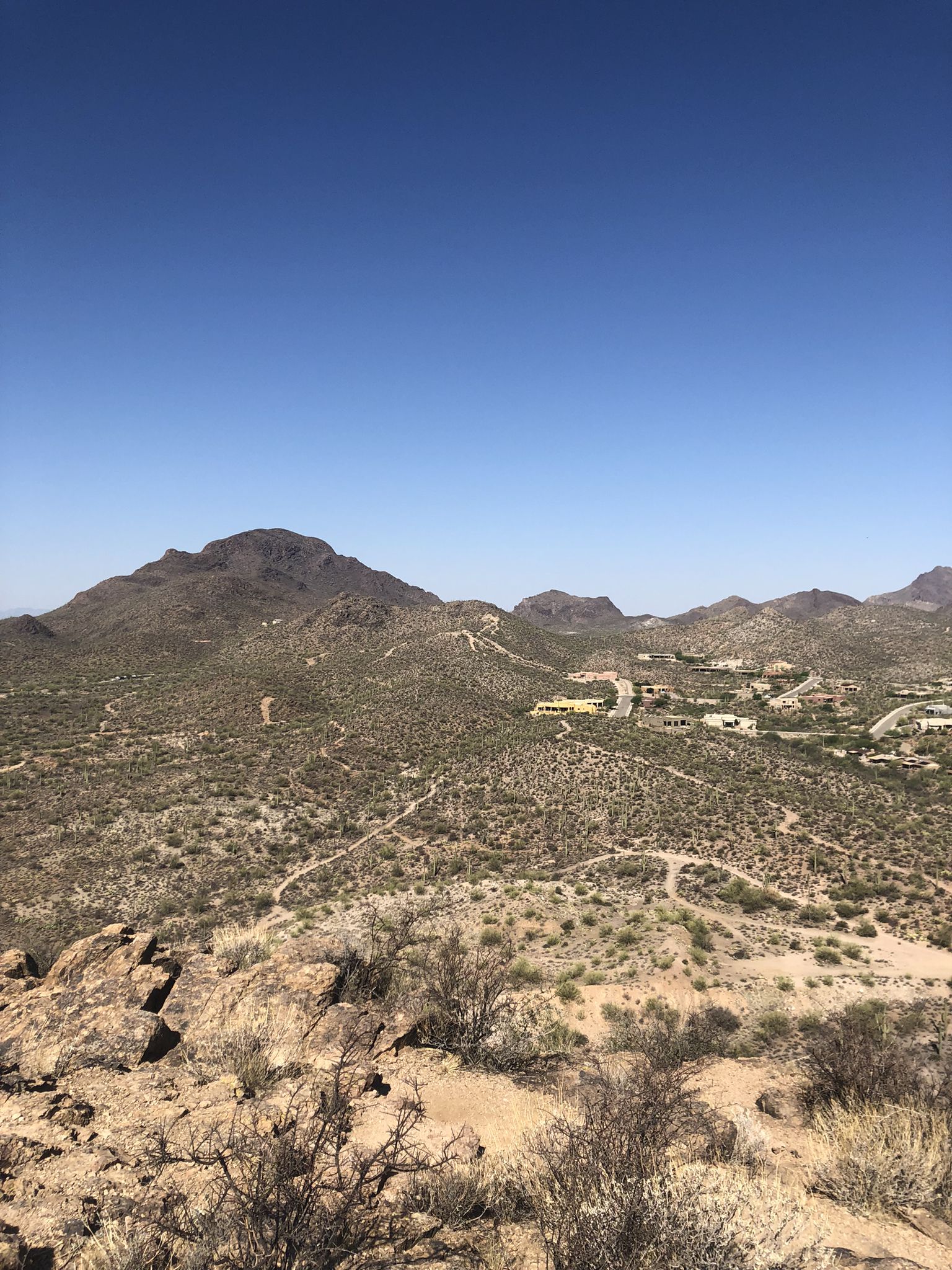 Vast desert landscape with mountains, sparse brush, and distant homes under clear sky. - Tecolote Trail