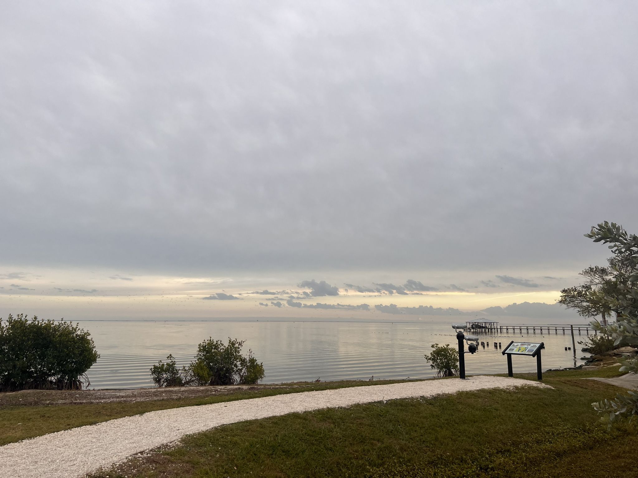 Overcast sky over calm water, with a gravel path leading to a distant pier. - Space View Park – Chain of Lakes Park loop from North U.S. 1/ Gloria Avenue (South East Corner)