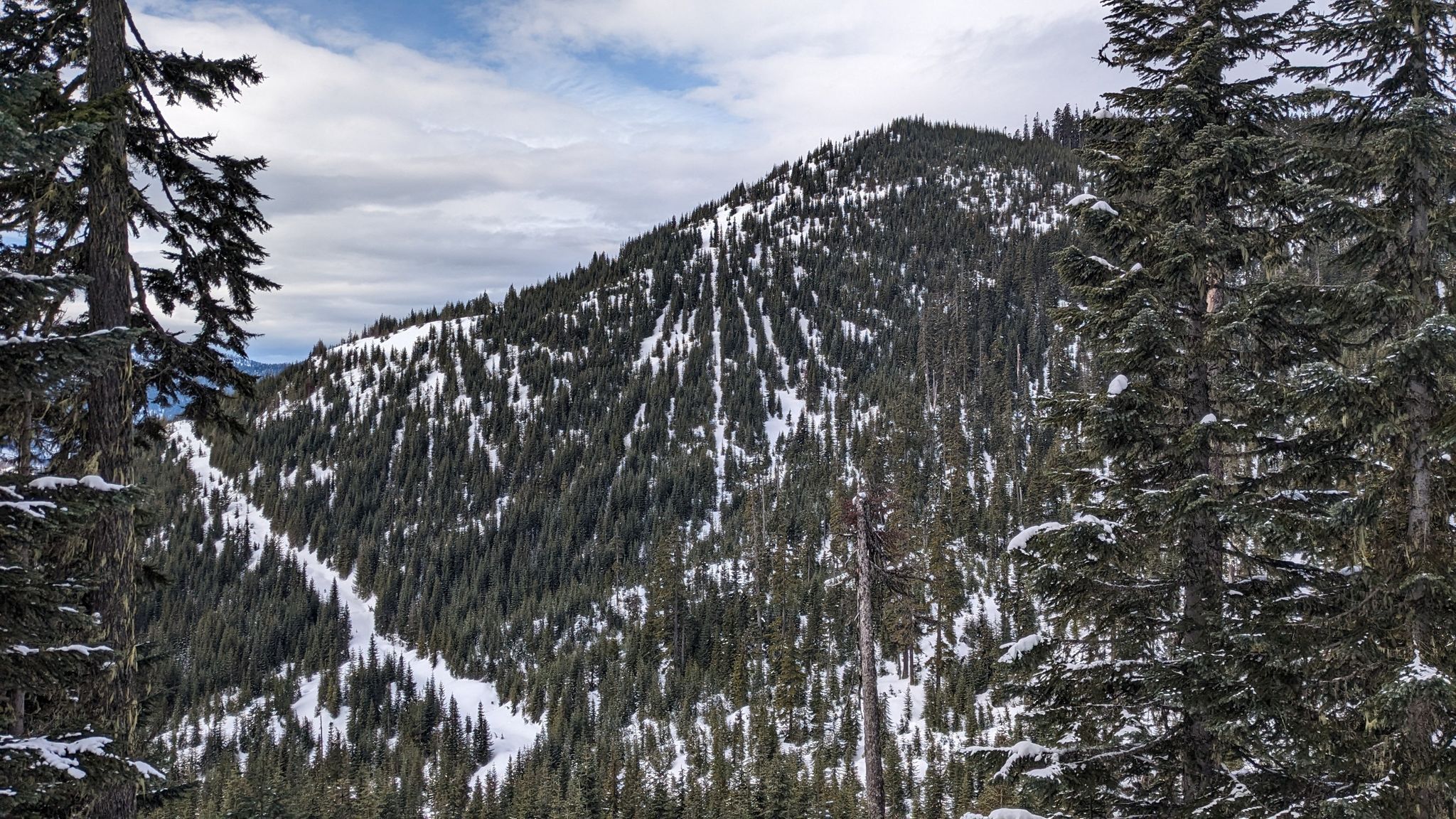 Overcast view of a snow-covered mountain with dense evergreen forests and ski runs. - Kendall Peak Lakes Trail