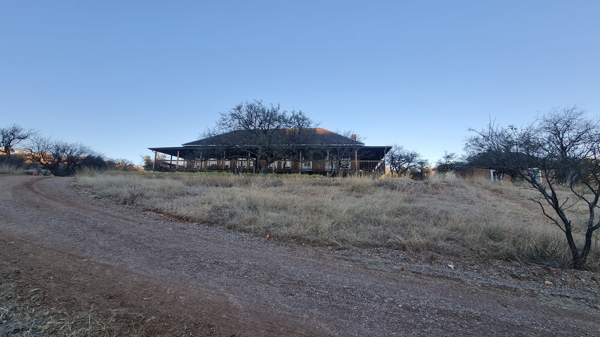 A large house with a porch on a dry grassy hill under a clear sky. - Kentucky Camp loop from Barrel Tank