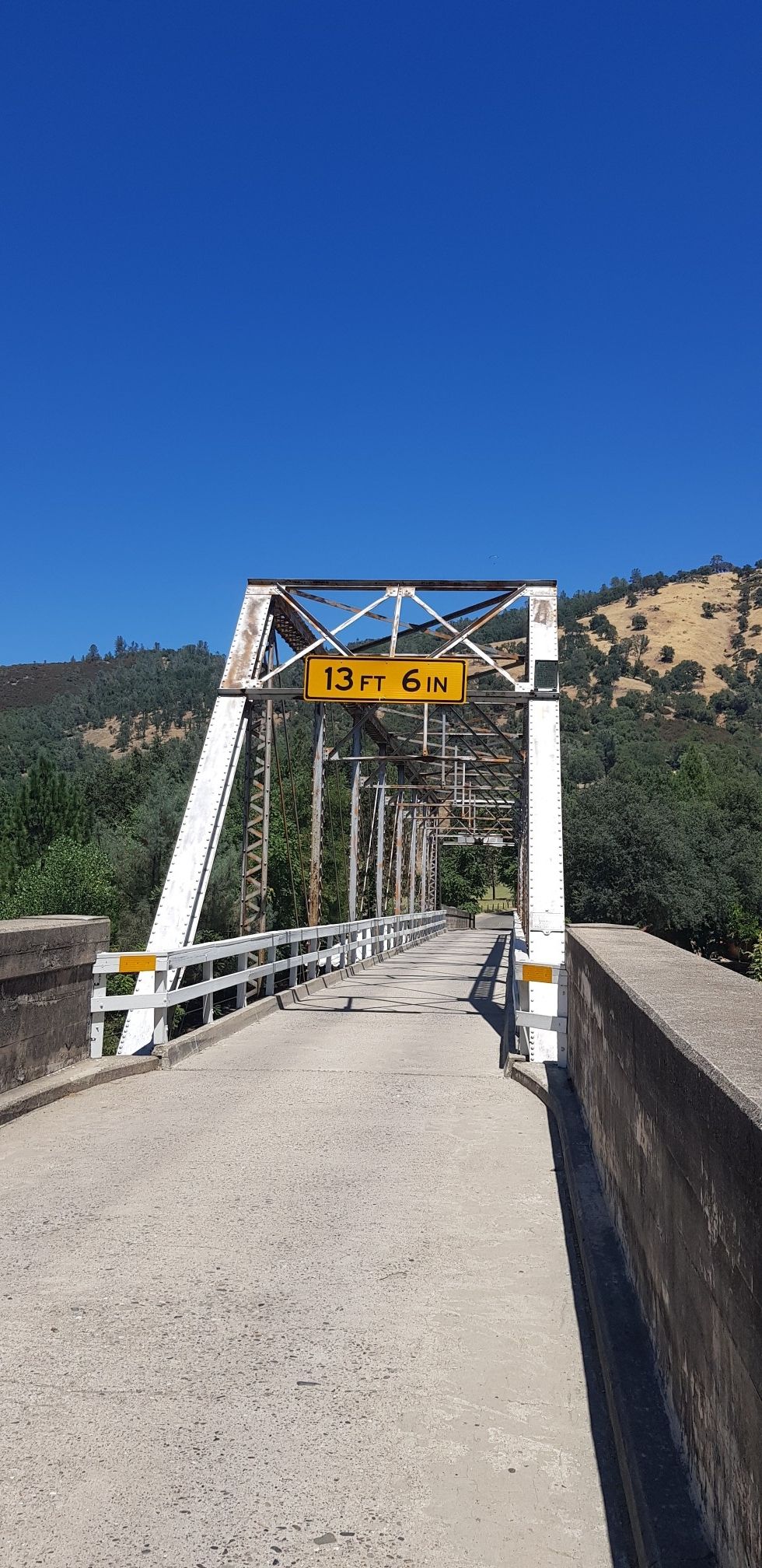 White metal truss bridge with a height sign under a clear blue sky. - Sutter's Mill Replica via Gold Discovery Trail