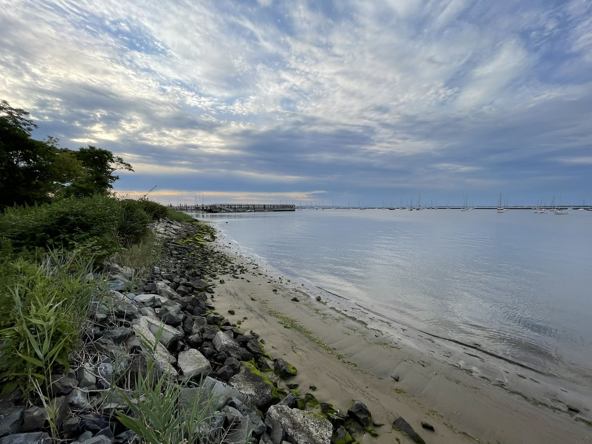 Rocky and sandy shoreline next to calm water under a cloudy sky. - Shrewsbury River – Navesink Beach loop from Belford