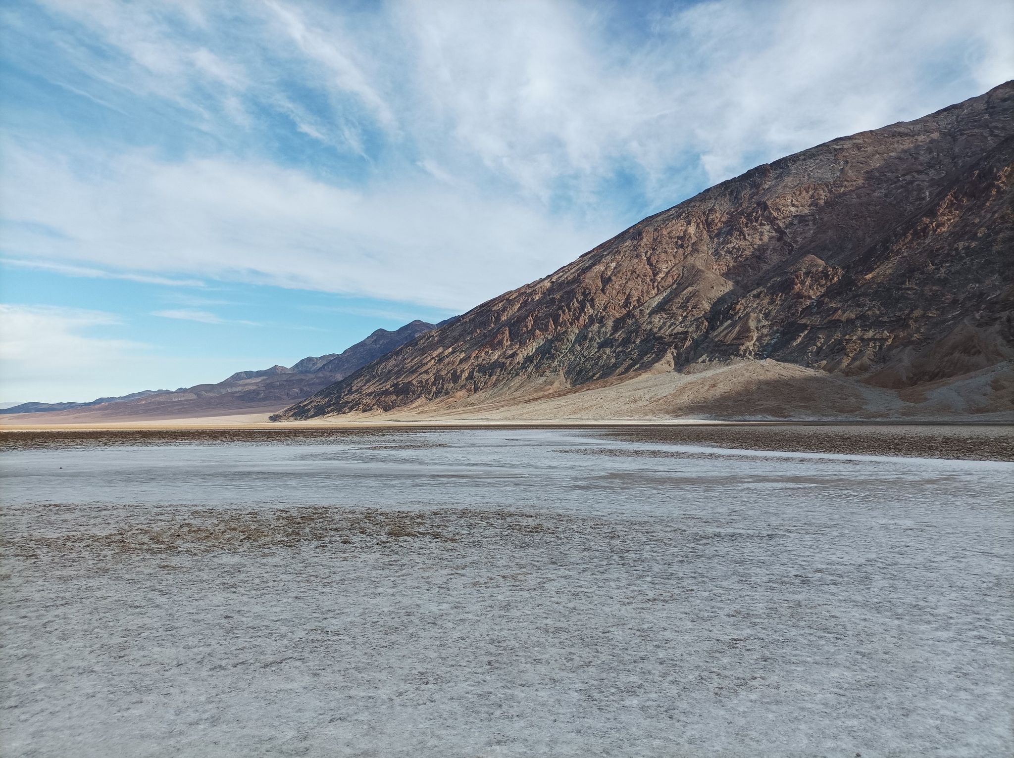 Expansive white salt flat stretching towards distant mountains under a blue sky. - Badwater Basin Salt Flats Trail