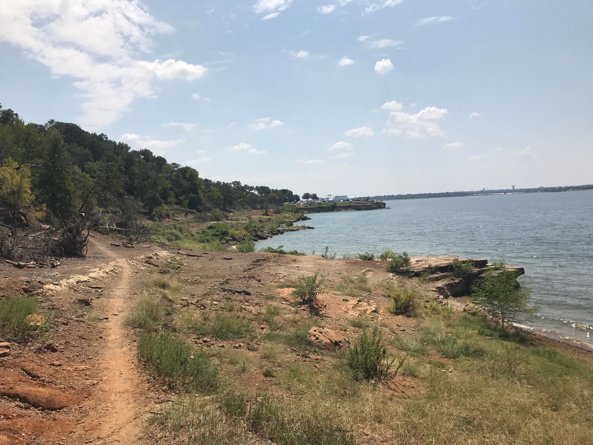 Dirt path along a lake shore with green trees under a partly cloudy sky. - Northshore Trail
